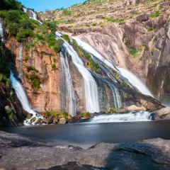 La cascada Fervenza se despliega en múltiples hilos blancos sobre rocas rojizas y verdes, desembocando en un lago sereno.