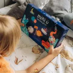 Dziecko trzyma pudełko z zestawem do kąpieli "mini ü". Na opakowaniu są kosmiczne motywy, które podpowiadają, jak używać kuli do kąpieli dla wspaniałej zabawy.