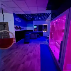 Nowoczesne spa z sauną, jacuzzi i wiszącym fotelem, oświetlone neonowym światłem.