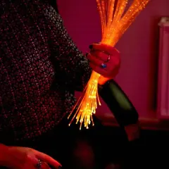 Une main tient un bouquet de fibres optiques lumineuses, évoquant l'univers apaisant du snoezelen.