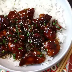 En skål med fluffigt ris toppad med glaserad teriyaki kyckling, strödd med sesamfrön och gräslök.