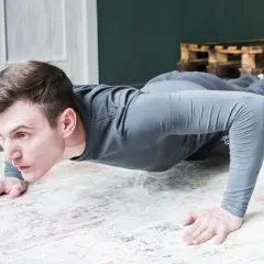 Un homme en tenue de sport fait des pompes tous les jours sur un tapis. Il est concentré et déterminé.