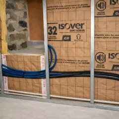Pose rail placo pour isolation acoustique Isover. Tuyaux bleus et noirs passent derrière.