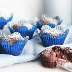 Kladdkakemuffins recept: Mjuka chokladmuffins i blåa pappersformar, pudrade med florsocker. En är uppskuren och visar en härligt kladdig insida.