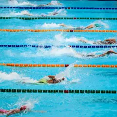 Zawodnicy w trakcie wyścigu pływackiego. Woda rozpryskuje się wokół nich, gdy wykonują ruchy. To dynamiczne sporty wodne po angielsku.