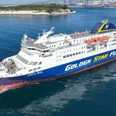 Prom "Andros King" Golden Star Ferries płynie po morzu. W tle widać port i góry.