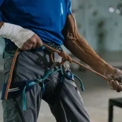 Mann mit bandagierter Hand prüft den klettergurt richtiger sitz und das Seil.