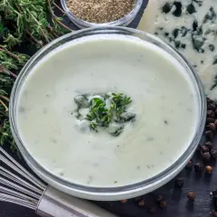 Crema suave con trozos de queso azul y tomillo fresco, lista para convertirse en una deliciosa salsa roquefort.