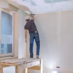 Pracownik na rusztowaniu szpachluje sufit. Poznaj atrakcyjną szpachlowanie cena za usługę.
