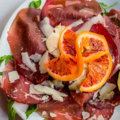 Bresaola co to? Delikatne plastry wędzonego mięsa wołowego, posypane parmezanem, z dodatkiem krwistych pomarańczy i cytryny.