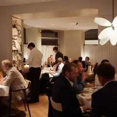 Gäster njuter av en middag på en elegant michelin restaurang i Karlstad. Servitörer serverar mat vid borden.