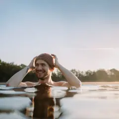 Uśmiechnięty mężczyzna w czapce zanurzony w zimnej wodzie, czerpiący radość z metody wim hof oddychanie.
