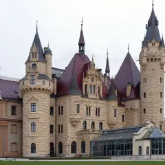 Zamek Książ, jeden z najpiękniejszych pałaców w Polsce, z licznymi wieżami i czerwonymi dachami, otoczony zielenią.
