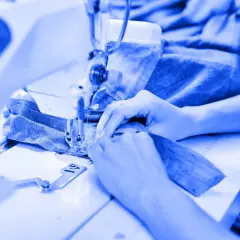Mains guidant du tissu bleu sous une machine à coudre, un aperçu de l'industrie du vêtement en pleine action.