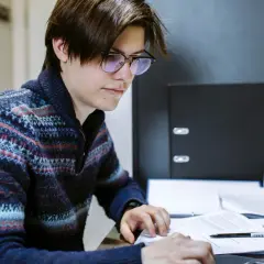A young man with glasses studies documents, working towards his online public administration certificate.
