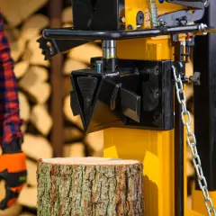 Żółta łuparka do drewna Cedrus gotowa do pracy. Obok pień drewna, w tle stos polan.