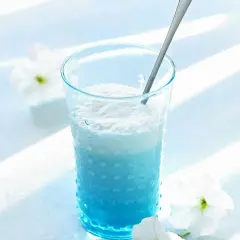 Ein erfrischender Blue Curacao Cocktail in einem strukturierten Glas, garniert mit weißen Blüten.
