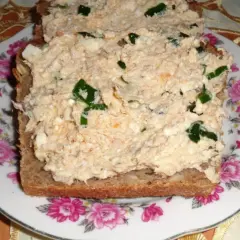 Pyszna pasta z makreli i twarogu z zieloną cebulką na ciemnym chlebie, podana na talerzu z różami.