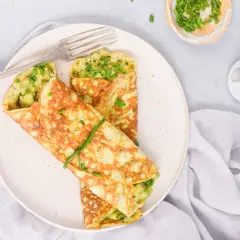 Omlet z awokado i szczypiorkiem na talerzu, obok widelca i miseczki ze szczypiorkiem.