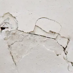Widoczne głębokie rysy skurczowe tynku, fragmenty odpadają, odsłaniając podłoże.