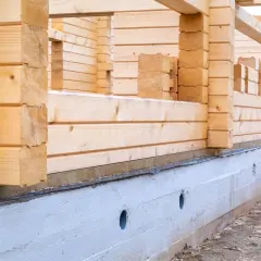 Budowa domu z bali w toku. Fundament betonowy, ściany z drewnianych belek. Zastanawiasz się, ile kosztuje postawienie domu z bali?