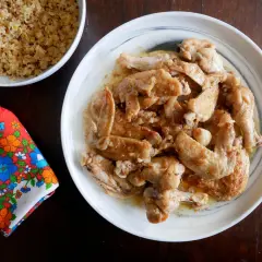 Alitas de pollo al ajillo, doradas y jugosas, servidas en un plato blanco. Acompañadas de quinoa y una servilleta colorida.