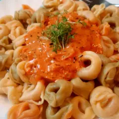 Kolorowe tortellini z kremowym sosem pomidorowym, udekorowane świeżymi ziołami. Pyszne danie gotowe do spożycia.