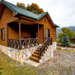 Urokliwa budowa domu drewnianego z kamienną podmurówką i werandą. W tle góry i inne drewniane domki.
