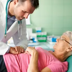 Lekarz w białym kitlu pochyla się nad pacjentką leżącą na kozetce.