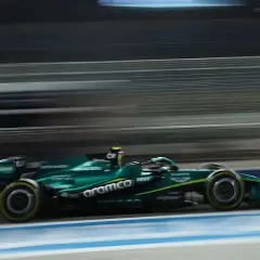 Un coche Aston Martin Honda verde compite a gran velocidad en una pista nocturna, con las luces y el fondo difuminados por el movimiento.
