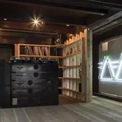 Theaster Gates studio: A DJ setup sits atop a dark wooden chest of drawers, surrounded by shelves of records and a striking neon art installation.