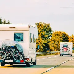 Kampery z rowerami na bagażniku jadą drogą. W tle lasy, jesienne drzewa. To widok jak z wakacji, może nawet z okolic roztocze lubelskie.