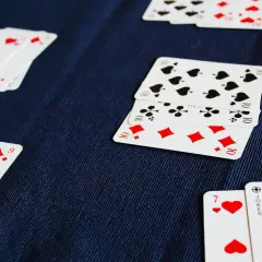 Karty do gry leżą na granatowym materiale. Widać 3, 5, 8 zasad gry.