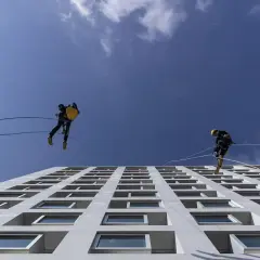 Lavoratori in corda assicurati da una linea vita tetto obbligatoria scendono lungo la facciata di un edificio moderno.