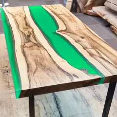 Tavolo con resina verde brillante tra venature di legno. La differenza tra levigatura e lucidatura è evidente nella finitura liscia e riflettente.