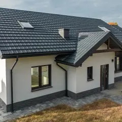 Nowoczesny dom z ciemnym dachem i solidnymi systemami rynnowymi, chroniącymi jego fundamenty.