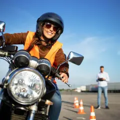 Uśmiechnięta kursantka na motorze, w kasku i kamizelce, uczy się jeździć. Zastanawia się, jakie prawo jazdy na motor 1000 będzie potrzebne.