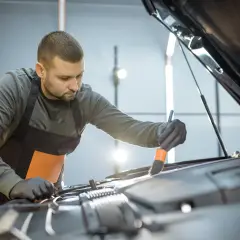 Mężczyzna w fartuchu i rękawiczkach precyzyjnie czyści silnik samochodu pędzelkiem. Dbałość o detale podczas mycia silnika.