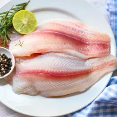Dos filetes de tilapia frescos, listos para cocinar, acompañados de romero, limón y granos de pimienta.
