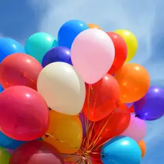 Kolorowe balony unoszą się na błękitnym niebie. Czy zwykłe balony można nadmuchać helem? Tak, jeśli są odpowiednio przygotowane.