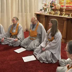 Menschen in buddhistischen Roben sitzen auf einem roten Teppich und lesen buddhistische Mantratexte.