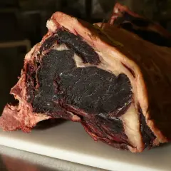 Gros morceau de viande maturée, prêt pour la cuisson. Sa couleur foncée et sa texture fibreuse promettent une saveur intense.