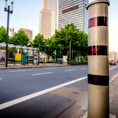 Blitzer am Straßenrand, bereit, Fahrer zu erwischen, die 31 kmh zu schnell auf der Autobahn fahren. Hohe Gebäude im Hintergrund.