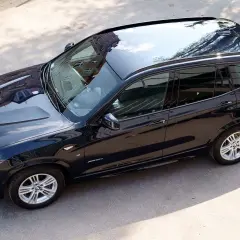 Ciemnogranatowe BMW X3, mocne auto tanie w utrzymaniu, lśni w słońcu. Widok z góry na błyszczący lakier i odbijające się budynki.