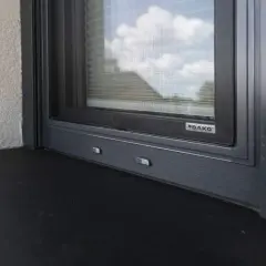 Szary parapet zewnętrzny pod oknem z moskitierą. Zastanawiasz się, czym przykleić parapet zewnętrzny blaszany?