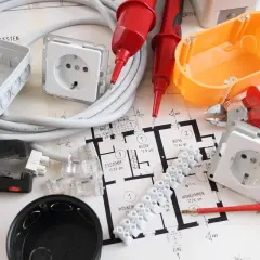 Narzędzia i materiały do wymiany instalacji elektrycznej bez kucia: przewody, puszki, gniazdka, zaciski, kombinerki, śrubokręt, miernik napięcia i plan mieszkania.