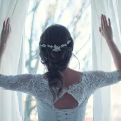 Elegancka fryzura dla świadkowej na wesele, z delikatną ozdobą we włosach, w białej koronkowej sukni, odsłaniająca zasłony.