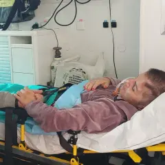 Pacjentka po pęknięciu tętniaka mózgu, z maską tlenową, trzymająca się bliskiej osoby. Rokowania niepewne.