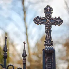 Ozdobny krzyż na tle nieba i drzew.