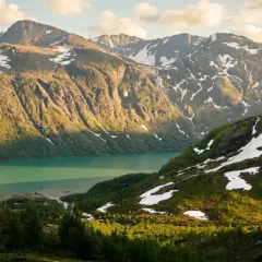 Majestatyczne góry Jotunheimen, jezioro o turkusowej barwie i zielone zbocza z resztkami śniegu.